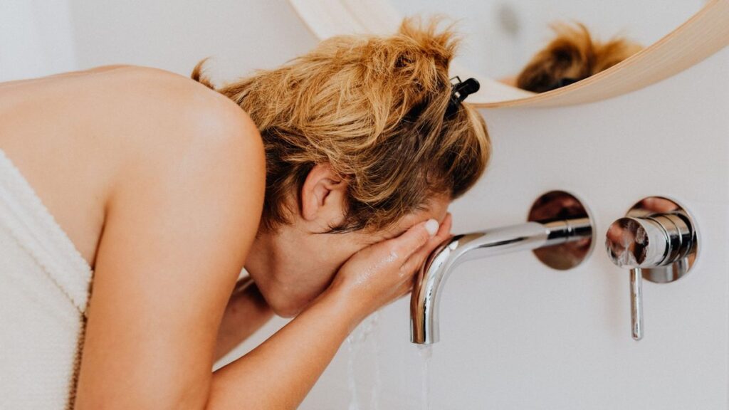 Femme se rinçant le visage au-dessus d'un lavabo